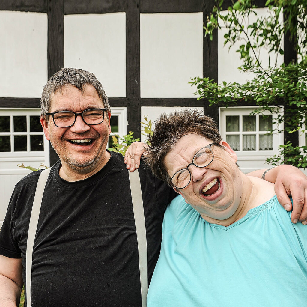 Zwei glücklichwirkende Menschen mit Behinderung liegen sich im Arm
