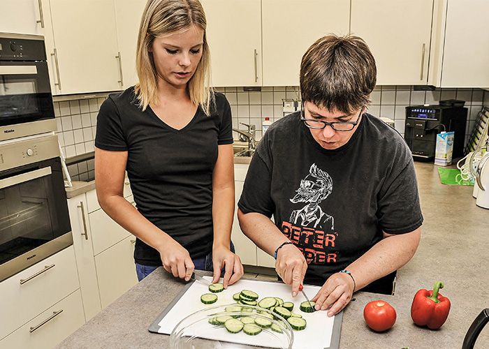 Betreuerin und Frau mit Behinderung schneiden in Küche Gurken