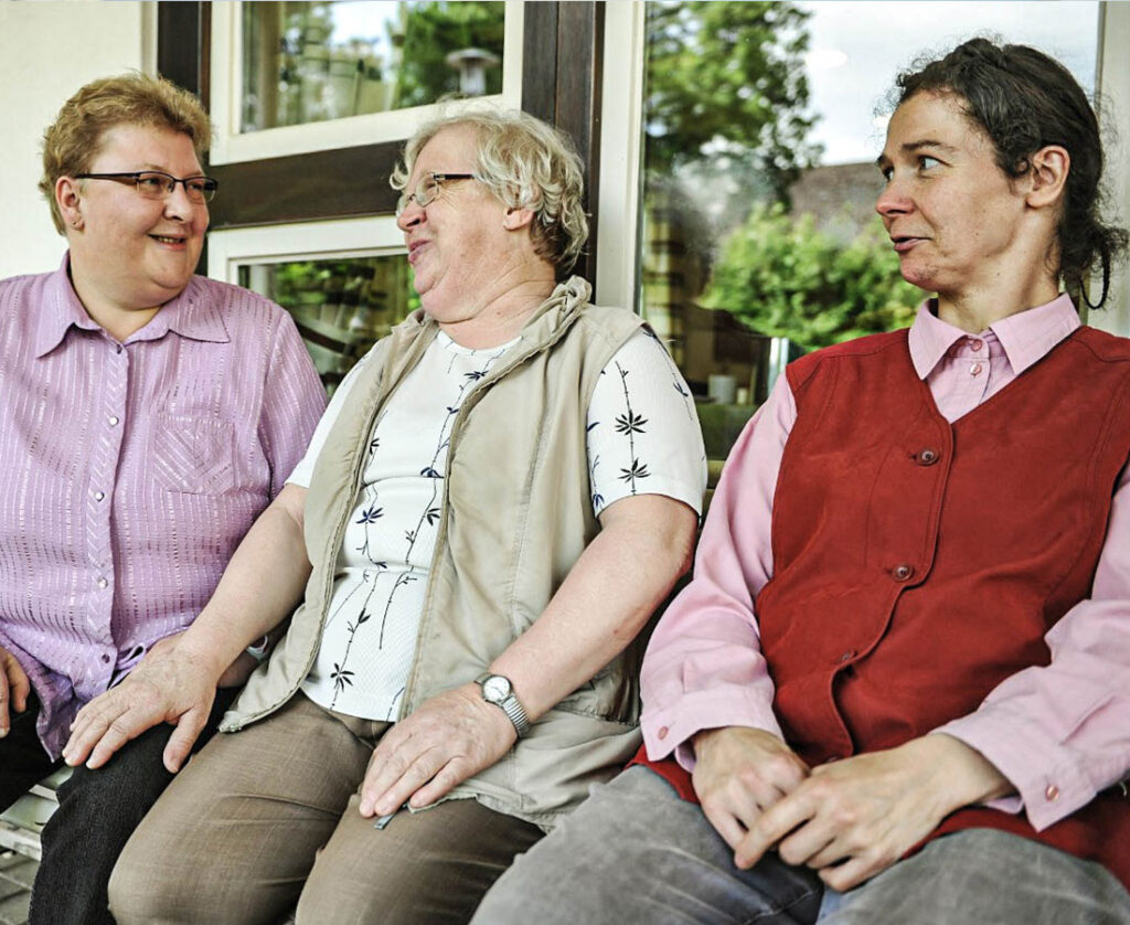 Drei Frauen sitzen auf Bank und schauen sich lachend an