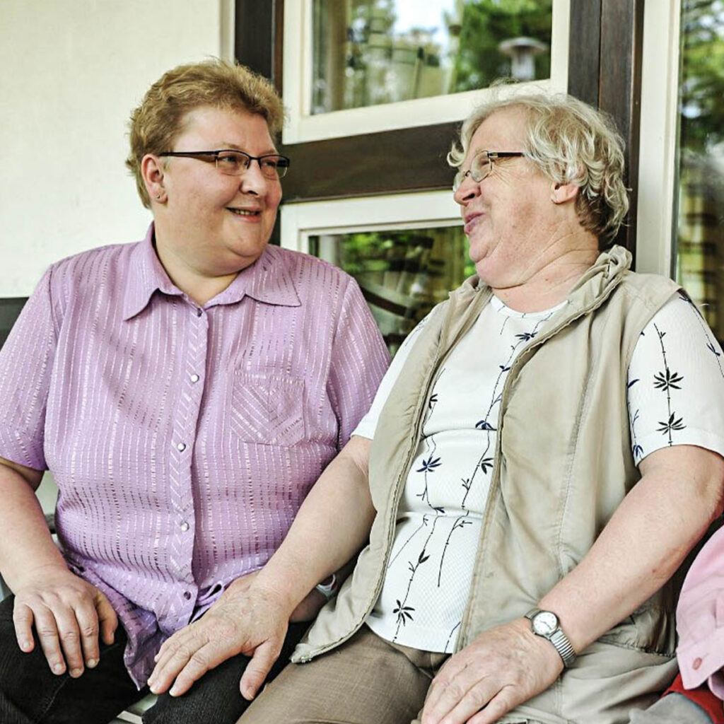 Zwei Frauen sitzen auf Bank und schauen sich lachend an