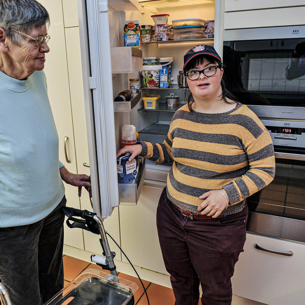 Zwei Frauen mit Behinderung stehen am geöffneten Kühlschrank