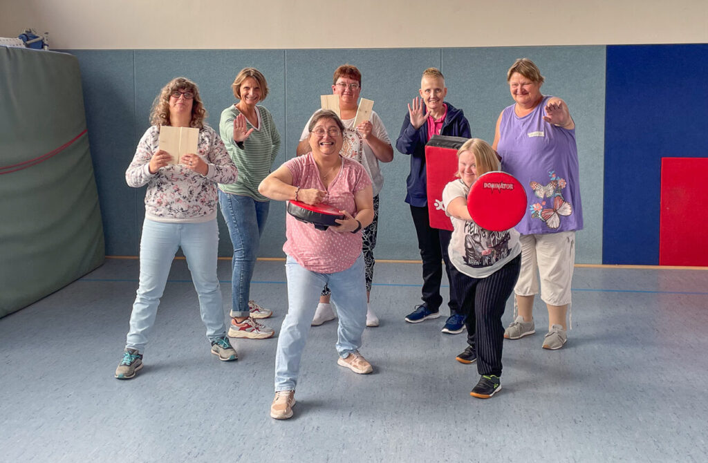 Gruppenbild von Frauen, die verschiedene Verteidigungsposen und Trainingsgeräte des WenDo-Kurses zeigen.